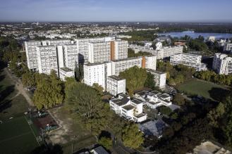 Vue d’en haut d’un quartier avec de grands immeubles, des arbres, des terrains de sport et un lac au fond.